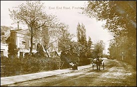 Left side, house behind trees,a horse cart in the middle of the road.